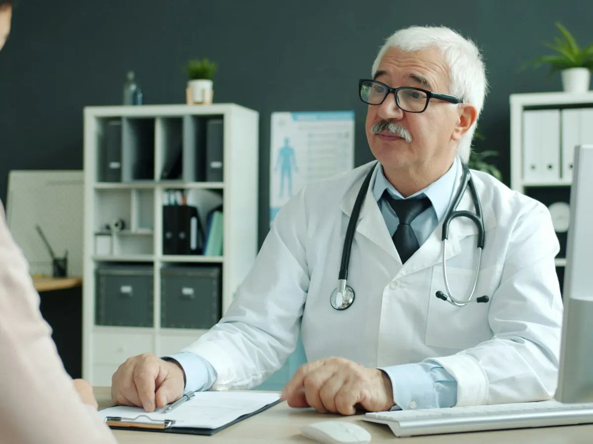 Physician in a white coat talking with a patient across a desk